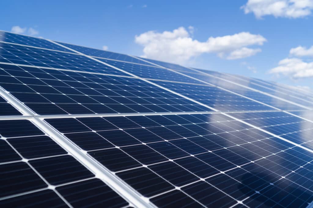 Panneaux Solaires Bleus Captant le Soleil et le Ciel Gros plan sur des panneaux solaires bleus captant la lumière sous un ciel bleu parsemé de nuages blancs, suggérant l'énergie renouvelable.