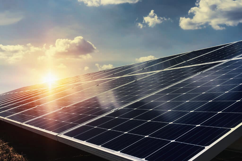 Panneaux Solaires Écologiques Capturant l'Éclat du Soleil Panneaux solaires alignés sous un soleil éclatant créant un fort effet de flare, avec un ciel bleu parsemé de nuages.