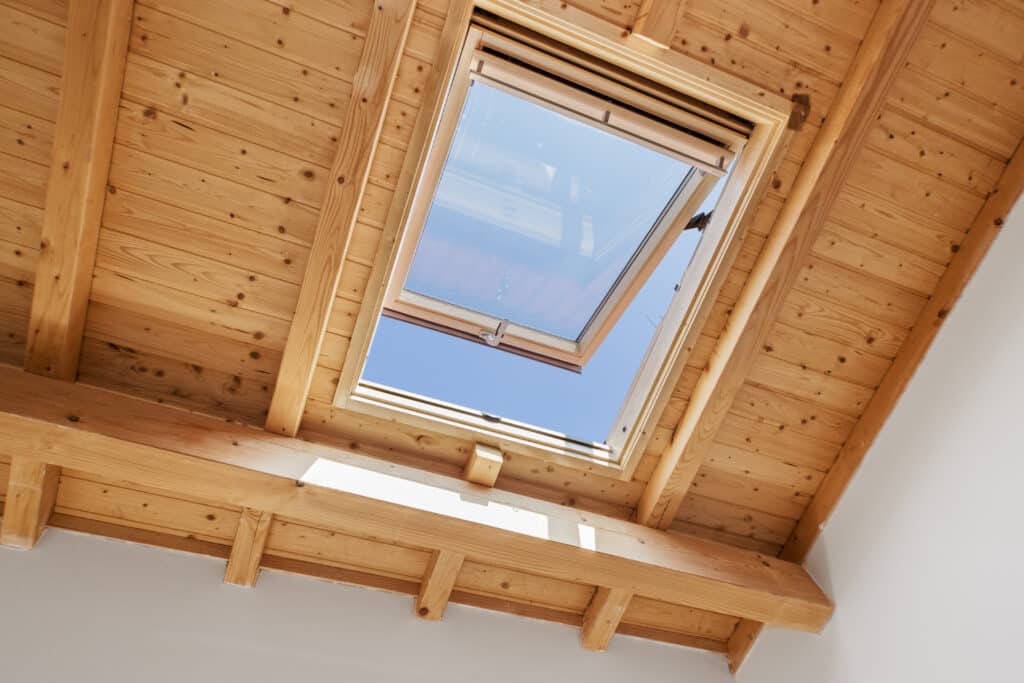 Fenêtre de Toit et Plafond en Bois : Luminosité Naturelle Fenêtre de toit ouverte dans un plafond en bois clair, offrant une vue sur le ciel bleu et la lumière naturelle.